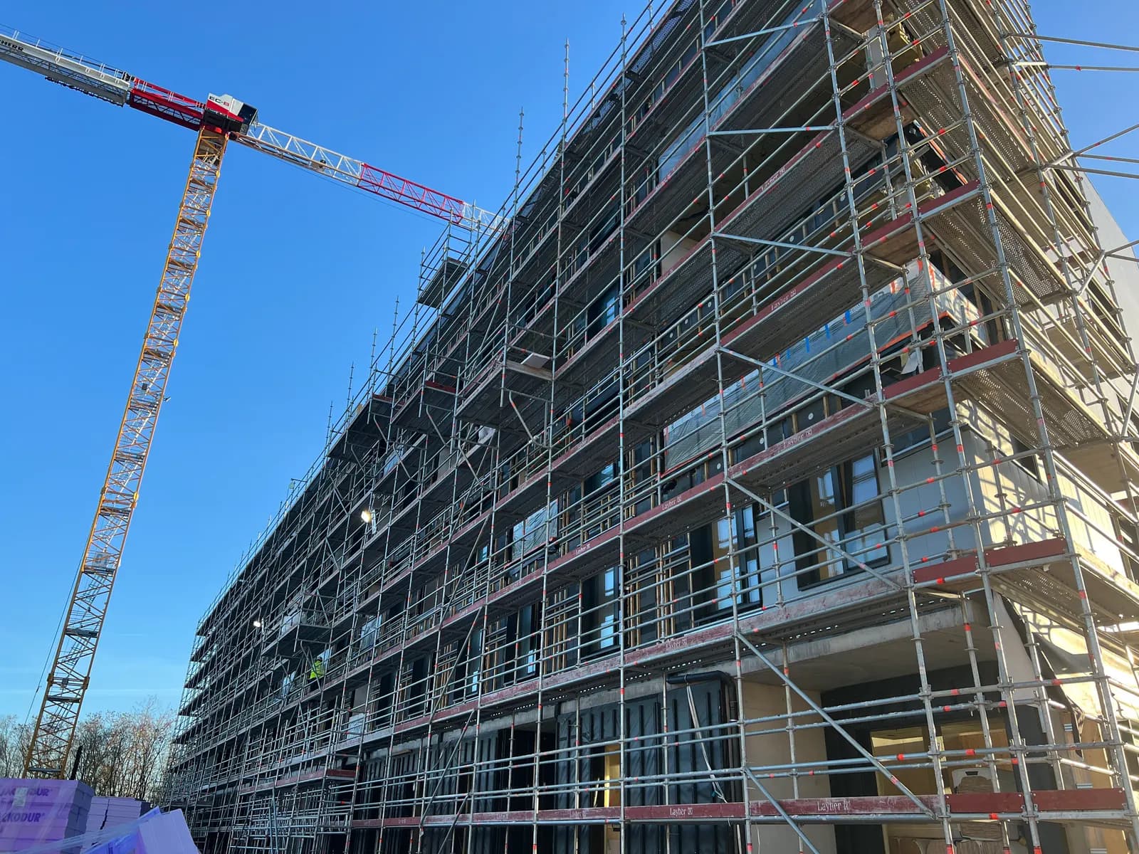 Programme neuf en cours de bardage sur l’un de nos chantiers actifs au Luxembourg — échafaudage et grue de levage, printemps 2026.